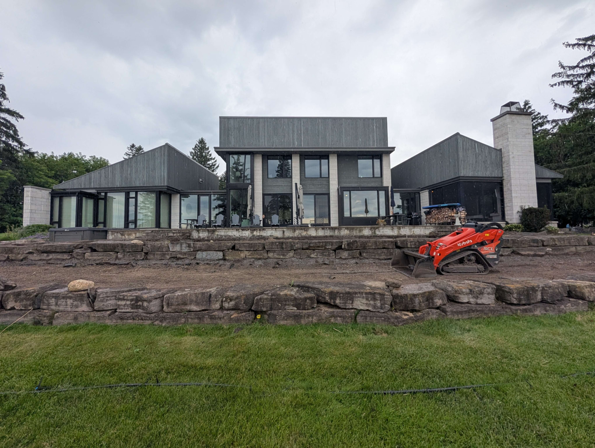 Compact track loader shaping a dirt terrace during a retaining wall build