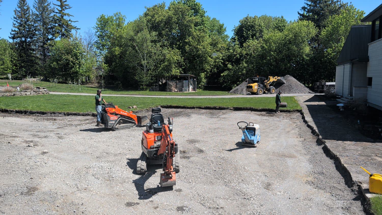 Mini excavator, track loader and plate compactor removing an old gravel driveway to make way for new lawn