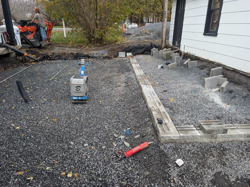Compacted clear stone base with plate compactor, drain pipe and first course of retaining wall block