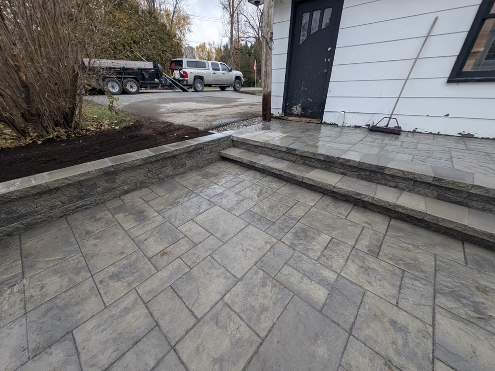 Finished interlock patio with steps up to the garage door and a capped retaining wall