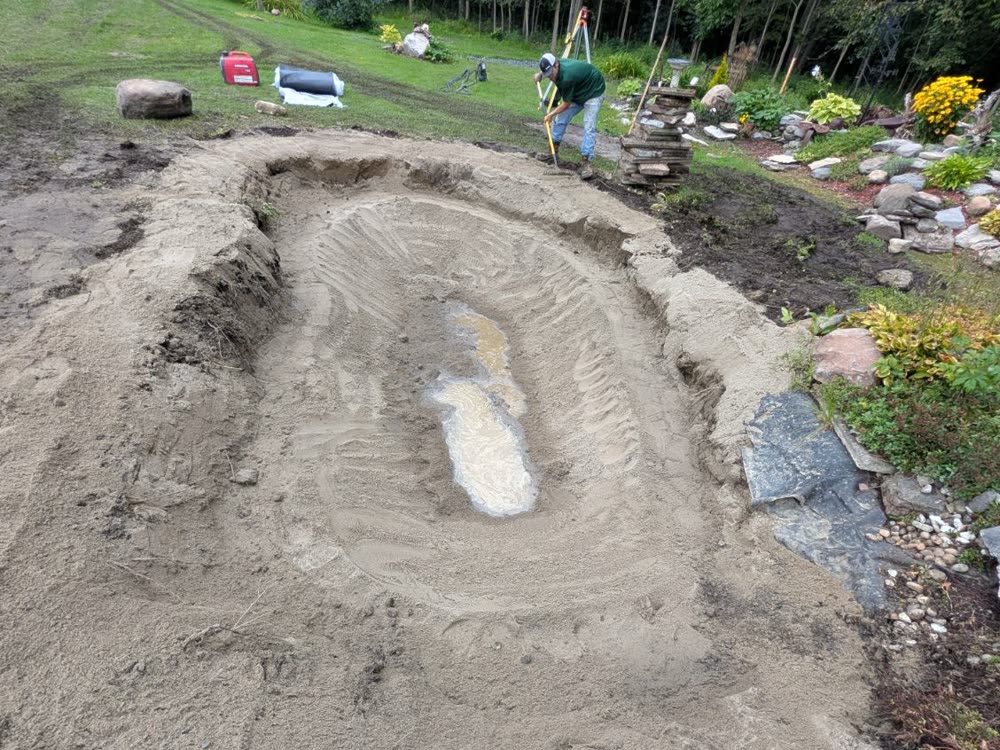Crew member raking a sand base inside a newly shaped pond
