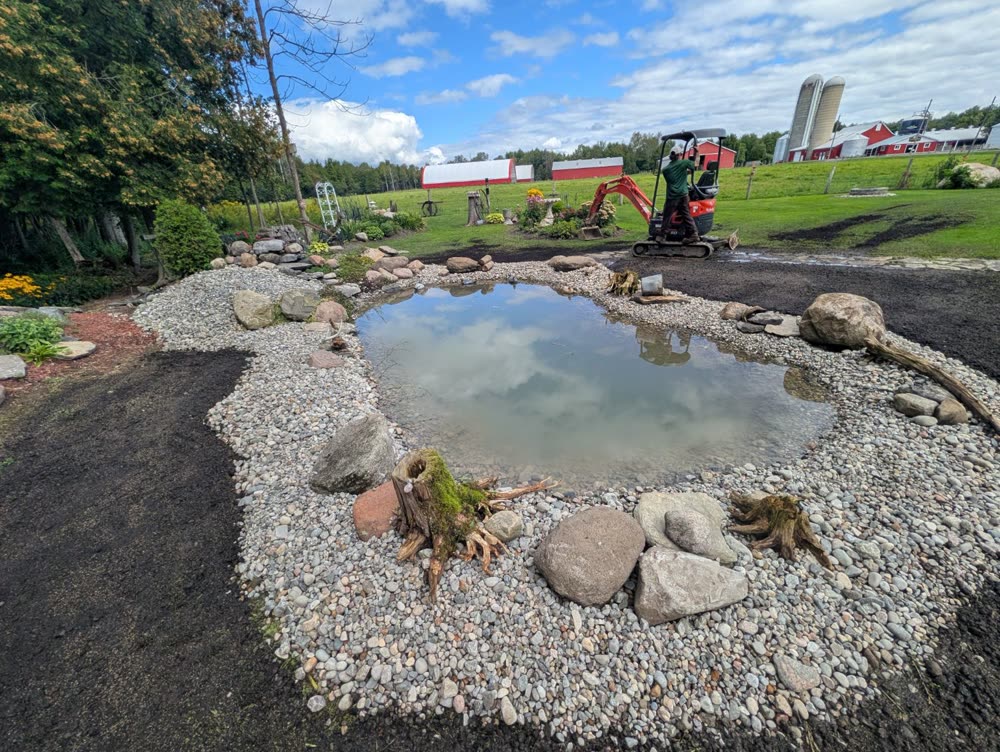 Finished backyard pond with river stone edging, boulders and driftwood stumps near Ingleside, Ontario