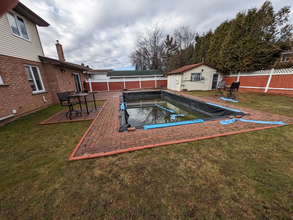 Old red interlock pool deck with heaved pavers and timber edging before the makeover