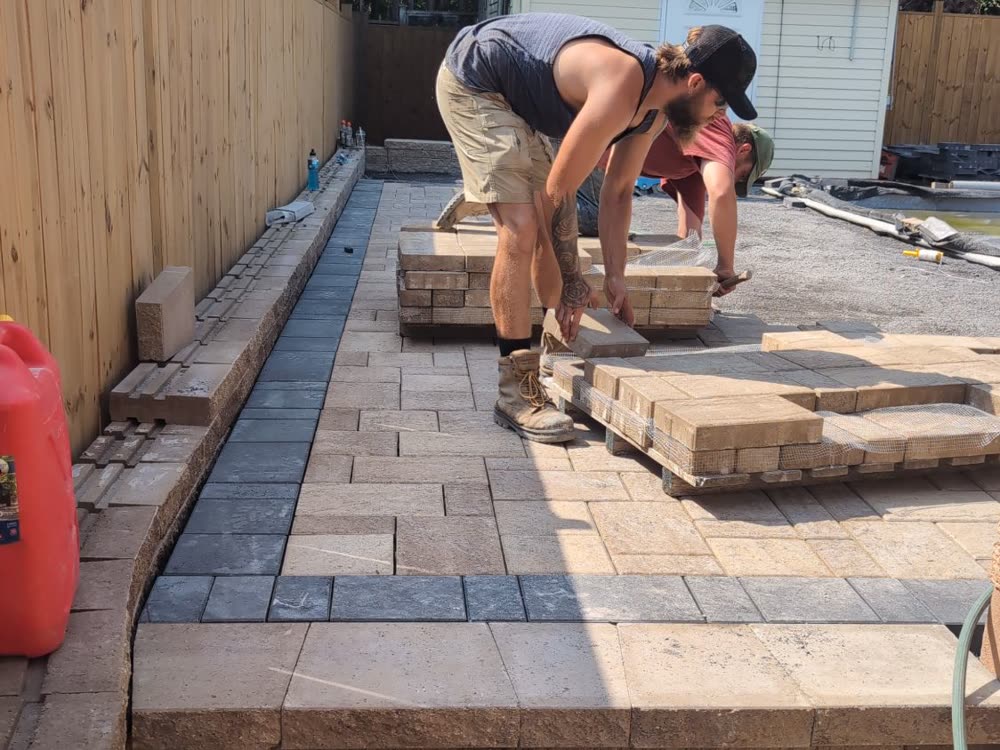 SD&G crew laying new pavers with a dark border band and steps along the fence