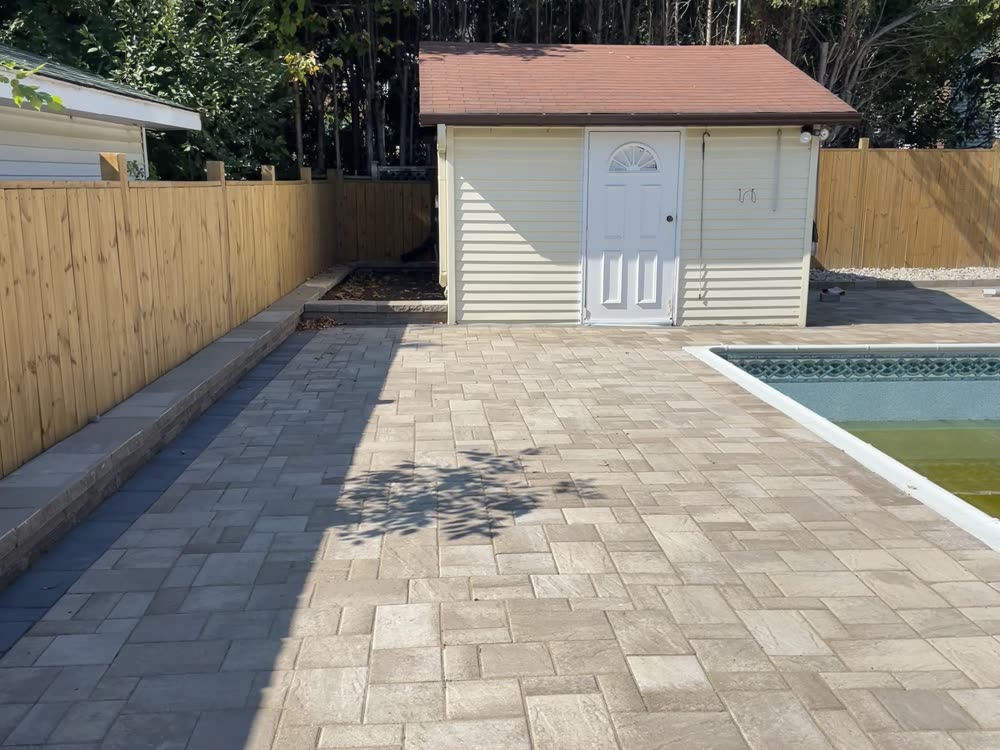 Finished interlock pool deck walkway with border band and low wall along the fence