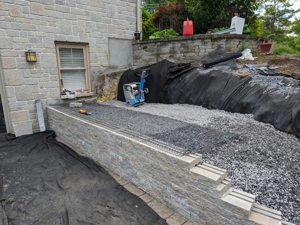 Segmental block retaining wall under construction with geogrid reinforcement laid over compacted clear stone backfill