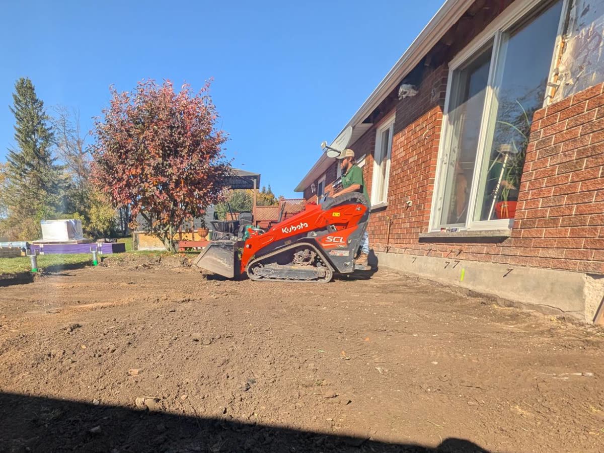 Track loader levelling the ground beside a brick house to prepare for a sunroom addition