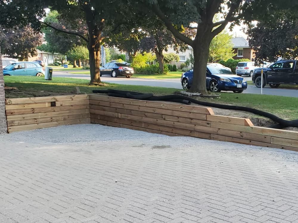 New stepped timber retaining wall along the edge of an interlock driveway, with drainage pipe ready behind it